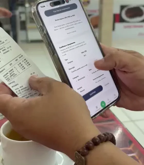 Mãos segurando o cupom da compra ao lado do celular com o lançamento pronto para confirmar